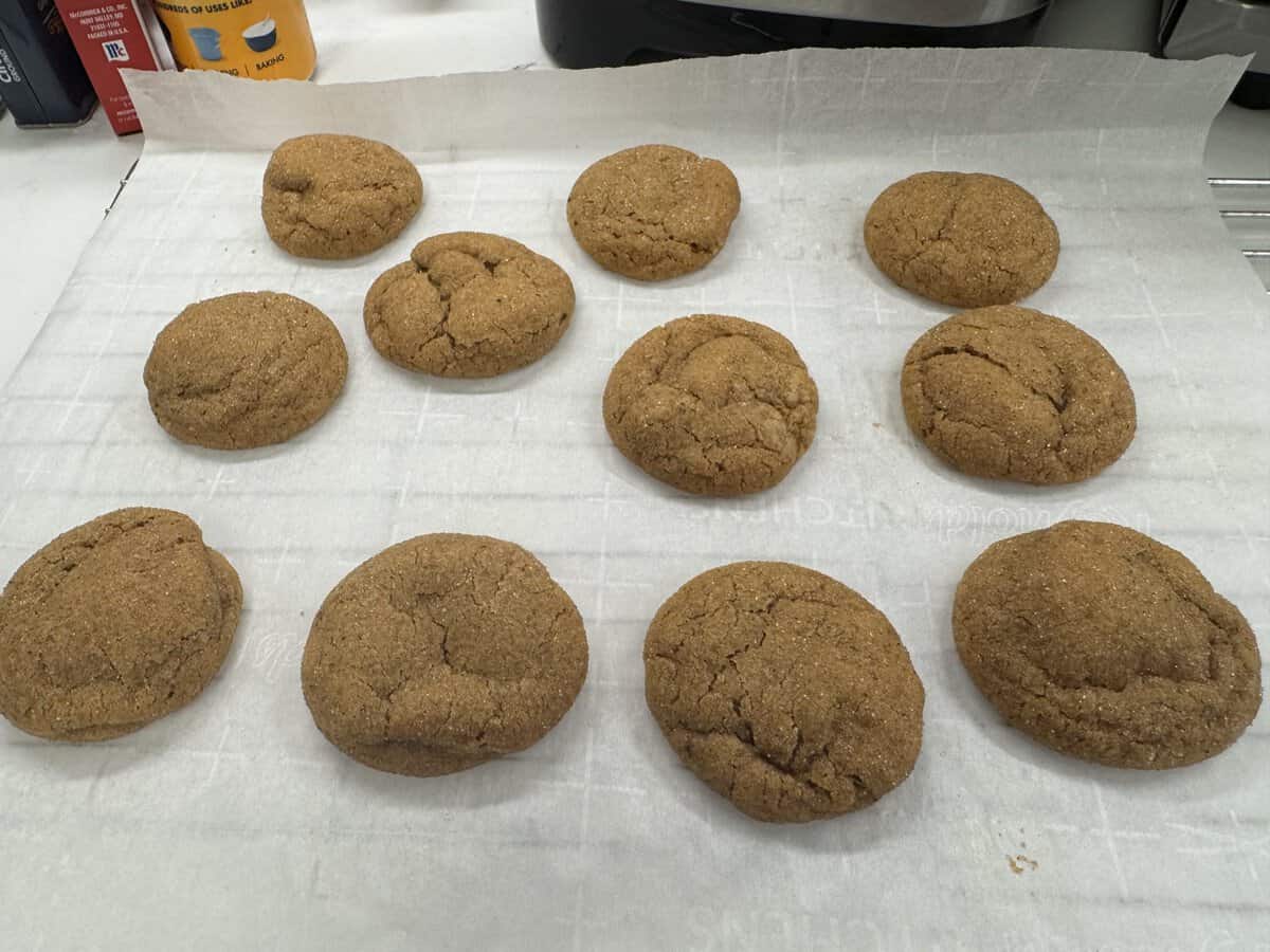 Eleven brown cookies on parchment paper, cooling on a rack in a kitchen setting.