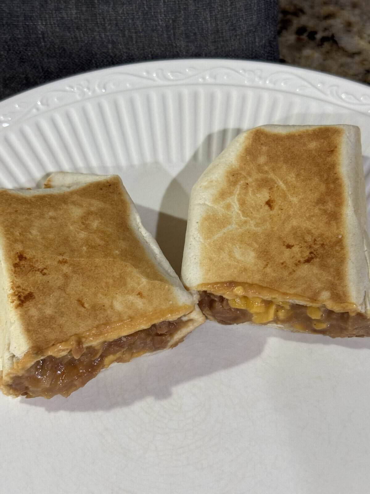 Two grilled burritos with cheesy filling are cut in half and placed on a white plate.
