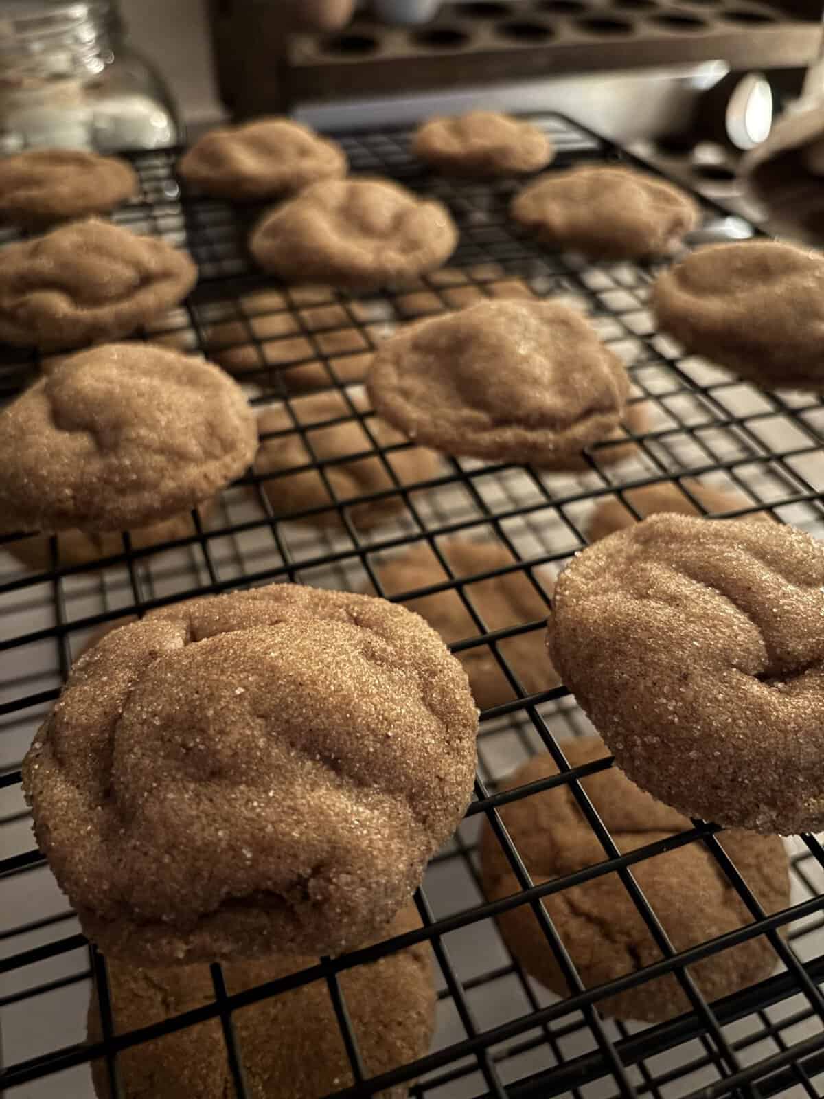 Close-up of freshly baked cookies cooling on a wire rack, with a jar and muffin tin blurred in the background.