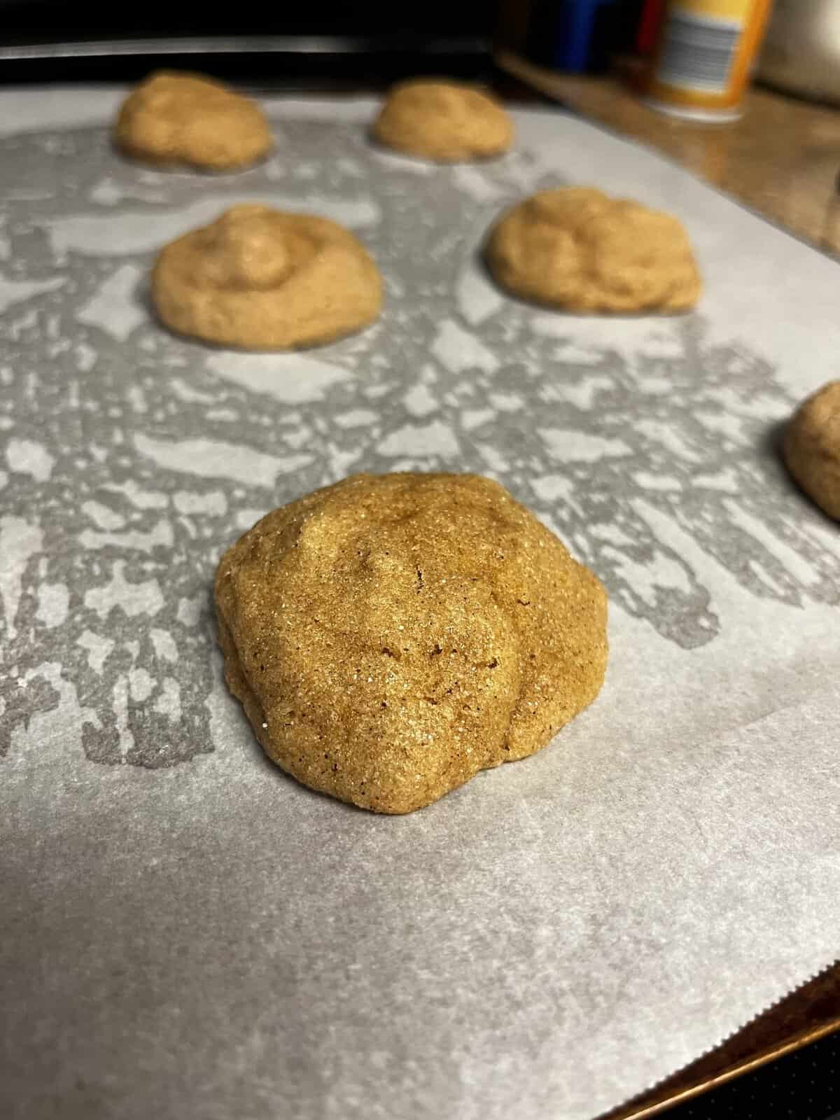 Close-up of unbaked cookie dough mounds on parchment paper-lined baking sheet, ready to be baked.