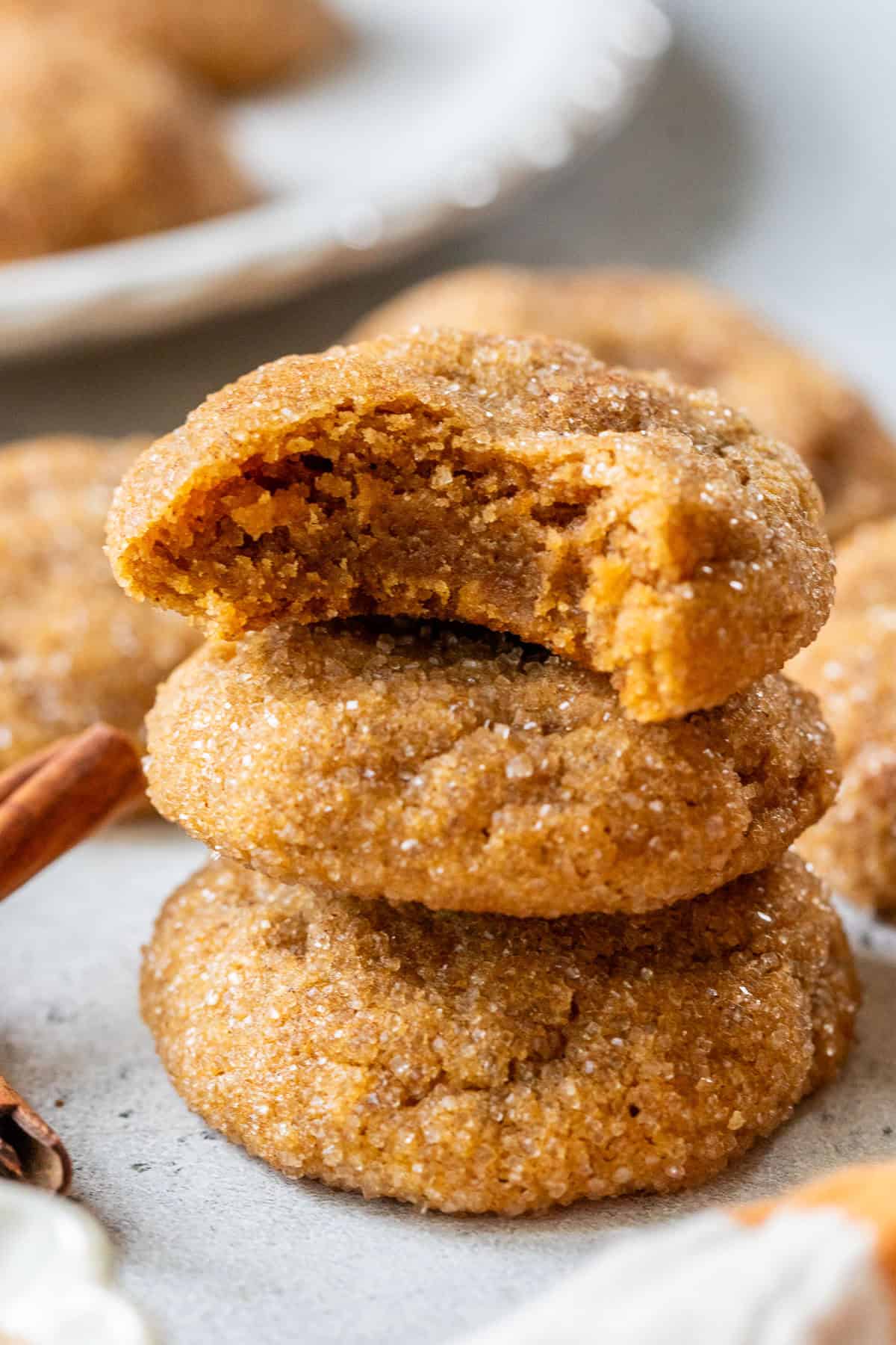 Three sugar-coated pumpkin spice cookies stacked, with the top cookie partially bitten, showing a soft, chewy center.