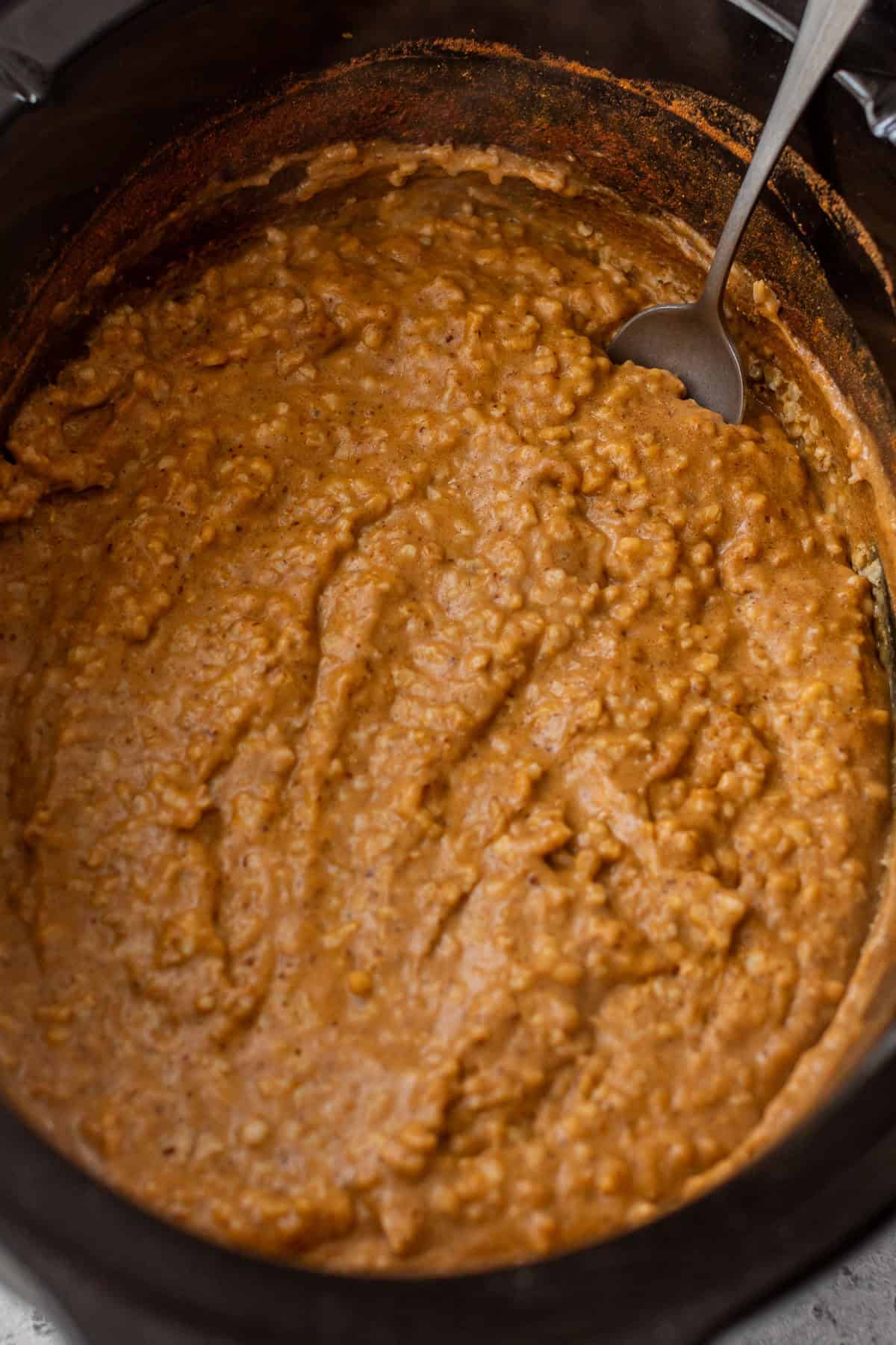 Spoon in a slow cooker filled with thick, creamy pumpkin oatmeal.