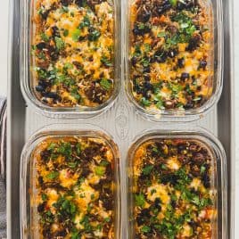 Four glass containers of cheesy casserole topped with chopped cilantro and black olives on a baking tray.