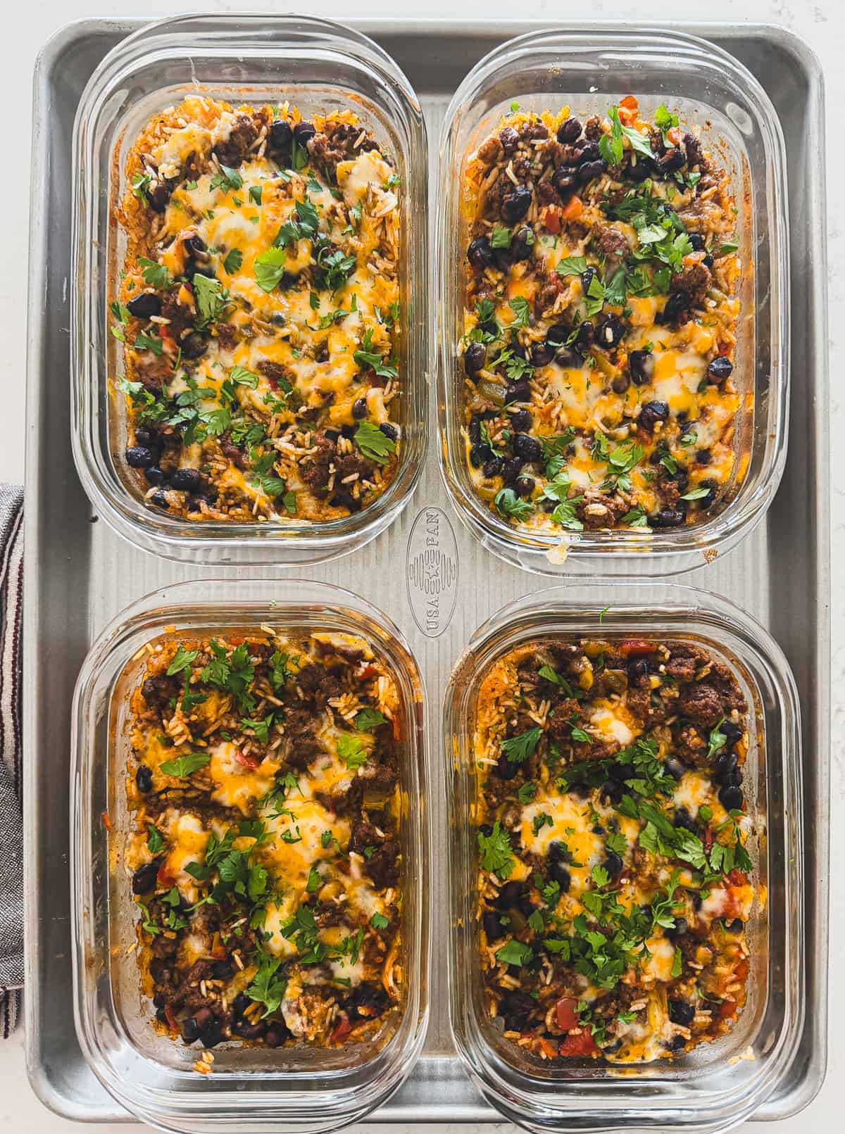 Four glass containers of cheesy casserole topped with chopped cilantro and black olives on a baking tray.