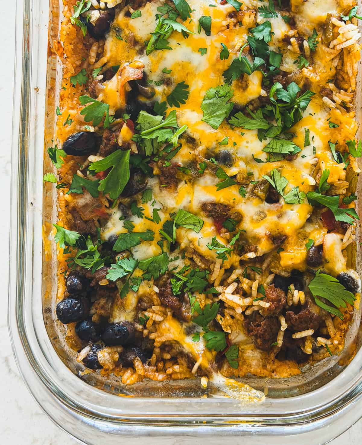 Casserole with melted cheese, black beans, rice, and fresh cilantro in a glass baking dish.