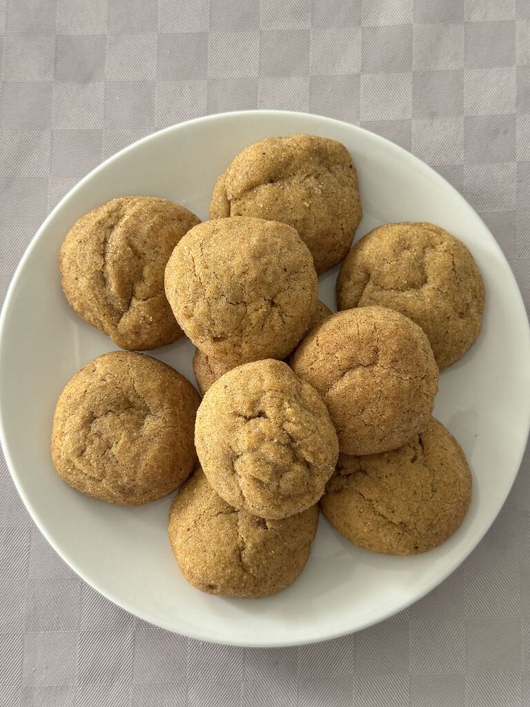 A white plate with ten golden-brown cookies on a light checkered tablecloth.