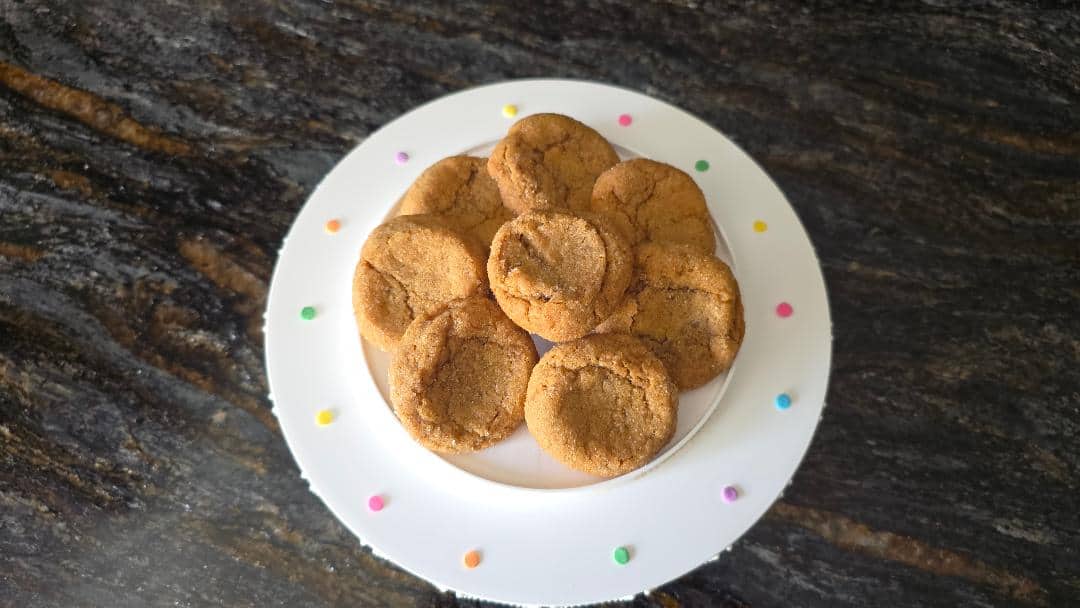 A plate of round, golden-brown cookies sits on a white stand decorated with colorful dots.