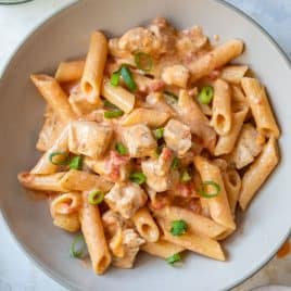 Bowl of creamy buffalo chicken pasta with tomatoes and green onions, seen from above.
