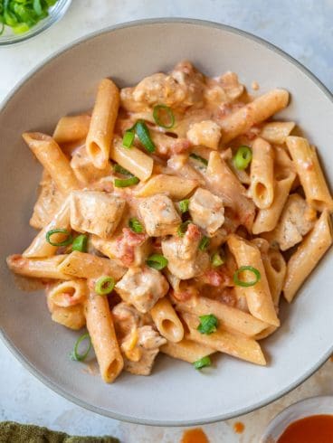 Bowl of creamy buffalo chicken pasta with tomatoes and green onions, seen from above.