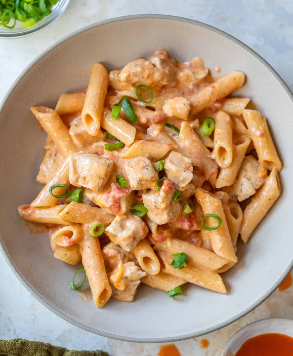 Bowl of creamy buffalo chicken pasta with tomatoes and green onions, seen from above.