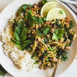 A plate of white rice and ground chicken stir fry with herbs, garnished with lime slices, basil, and cilantro.