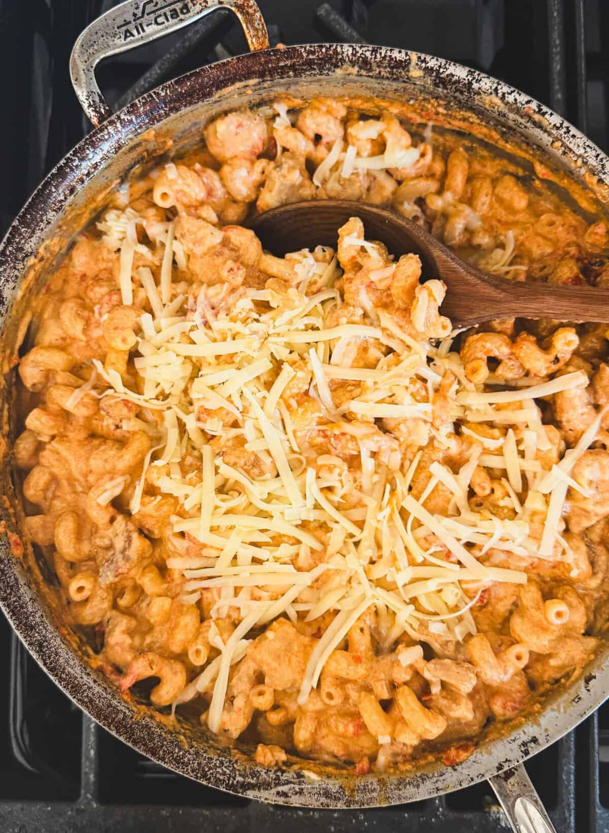 A pot of creamy macaroni and cheese topped with shredded cheese, with a wooden spoon resting inside.