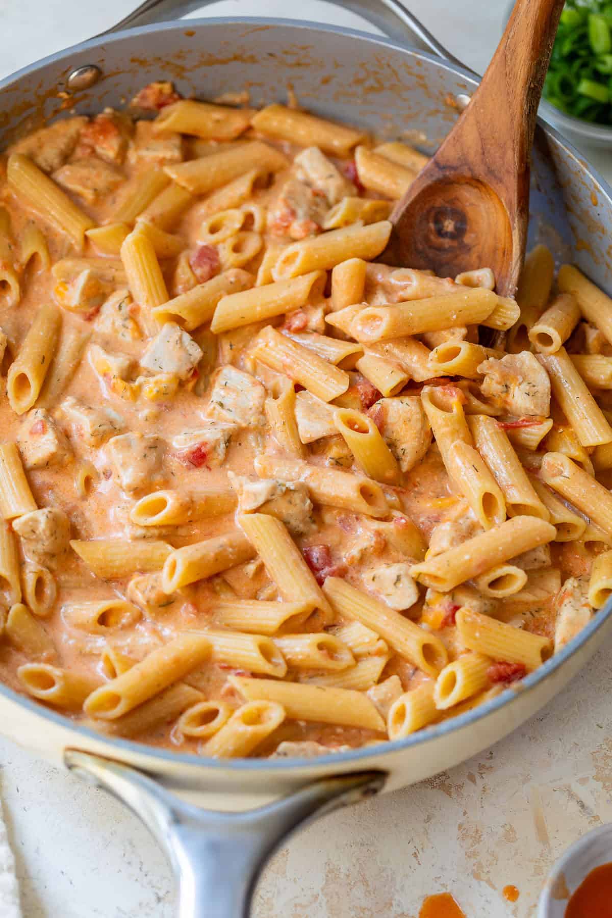 Buffalo chicken pasta in a skillet, stirred with a wooden spoon.