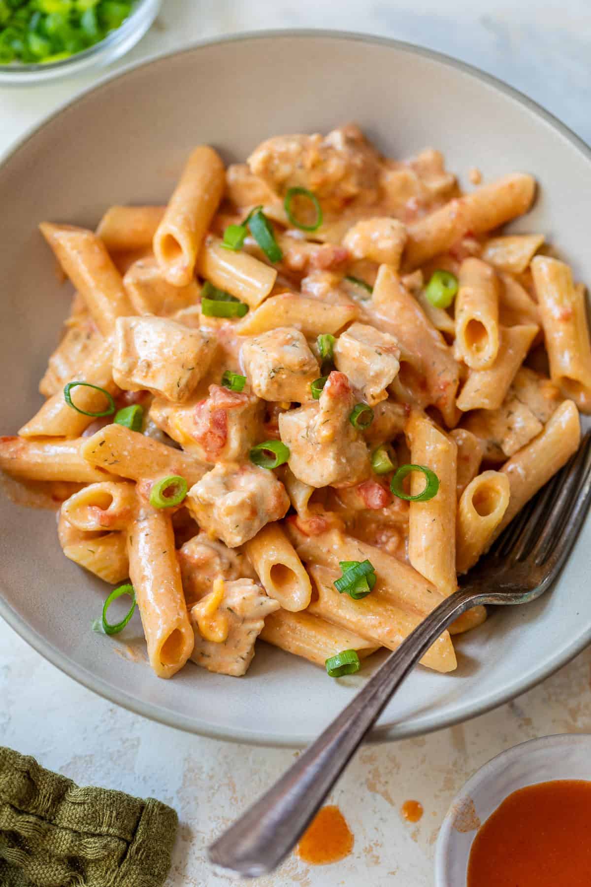Creamy buffalo chicken pasta with diced tomatoes, garnished with sliced green onions in a bowl with a fork.