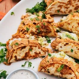 buffalo chicken tacos filled with shredded lettuce and a creamy filling, garnished with cilantro, served with a dip.