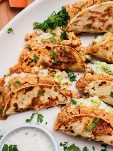 buffalo chicken tacos filled with shredded lettuce and a creamy filling, garnished with cilantro, served with a dip.
