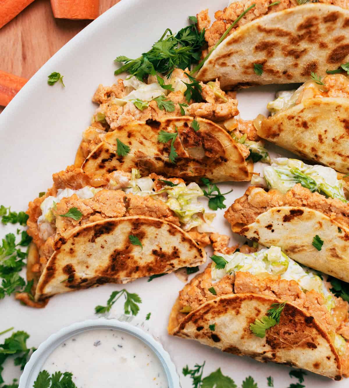 buffalo chicken tacos filled with shredded lettuce and a creamy filling, garnished with cilantro, served with a dip.
