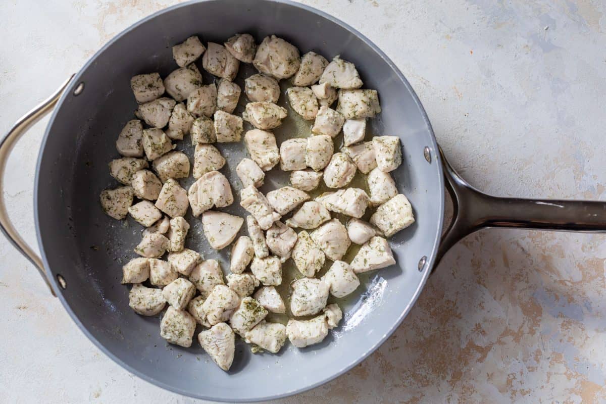 Cubed, seasoned chicken cooking in a large gray skillet on a light, textured surface.