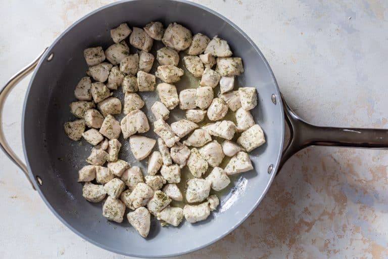 Cubed, seasoned chicken cooking in a large gray skillet on a light, textured surface.