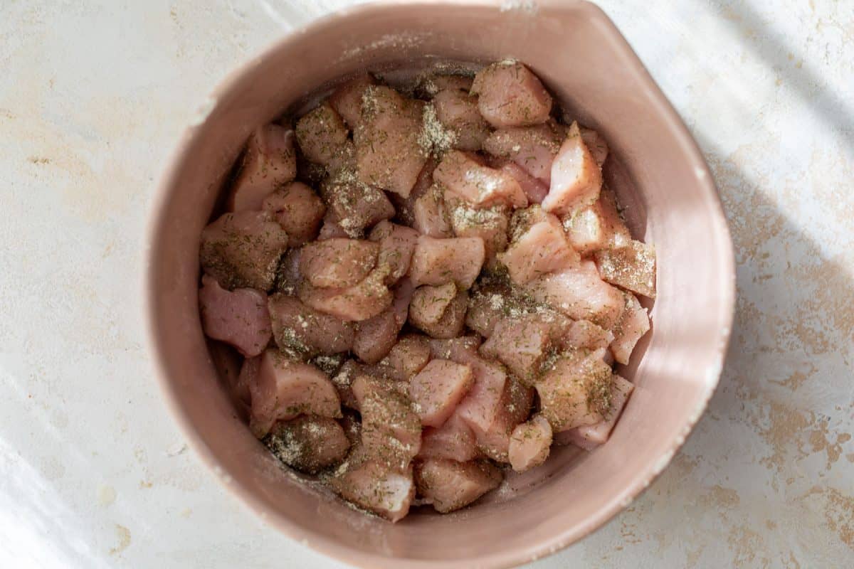Raw, seasoned chicken pieces in a pink bowl on a light-colored surface, ready to be cooked.
