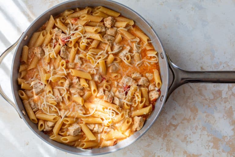 A skillet of creamy buffalo pasta with chicken chunks and shredded cheese on top.