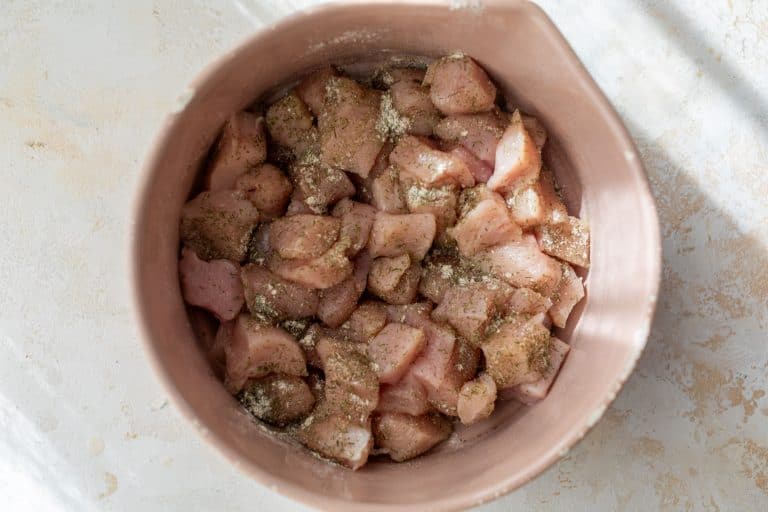 Raw, seasoned chicken pieces in a pink bowl on a light-colored surface, ready to be cooked.