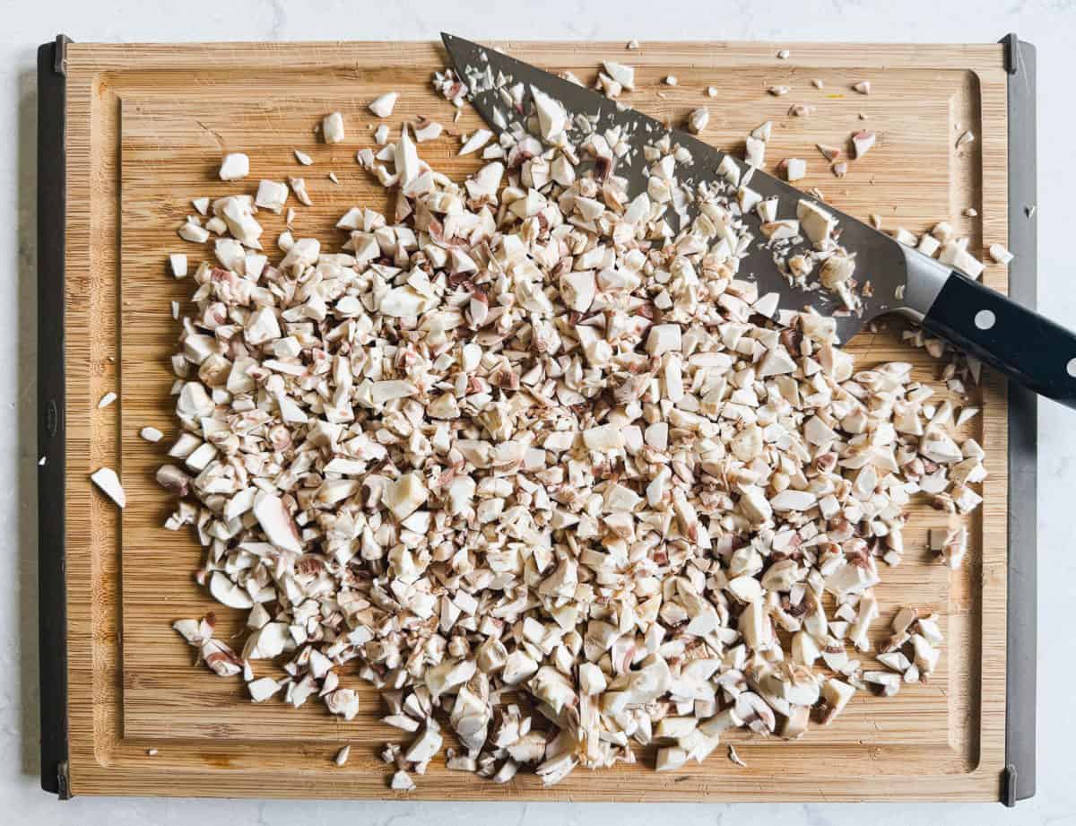 Chopped mushrooms and a knife on a wooden cutting board, viewed from above.