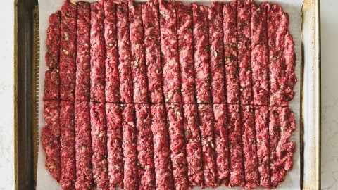 Raw ground beef pressed flat and cut into uniform strips on a parchment-lined baking sheet for gyro recipe.
