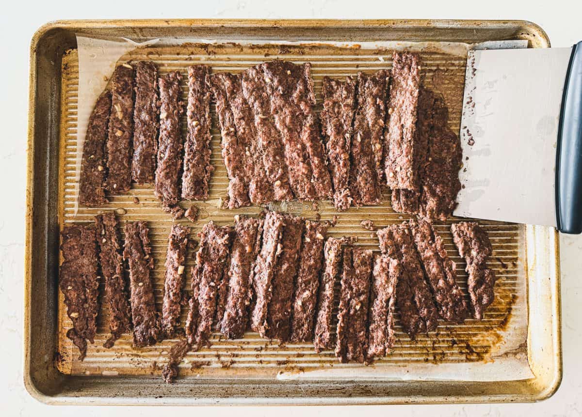 Sliced gyro meat on a baking sheet with a metal spatula on the right side.