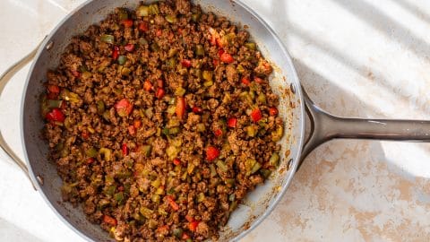 A skillet filled with seasoned ground beef, diced red and green bell peppers on a light countertop.