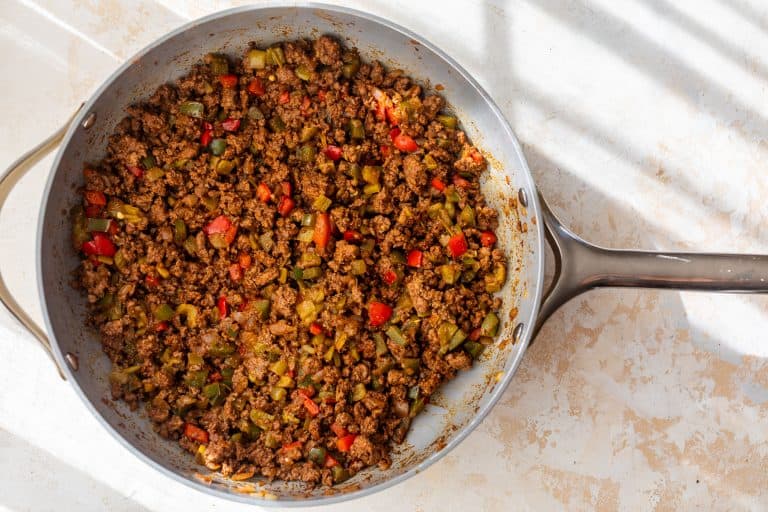 A skillet filled with seasoned ground beef, diced red and green bell peppers on a light countertop.