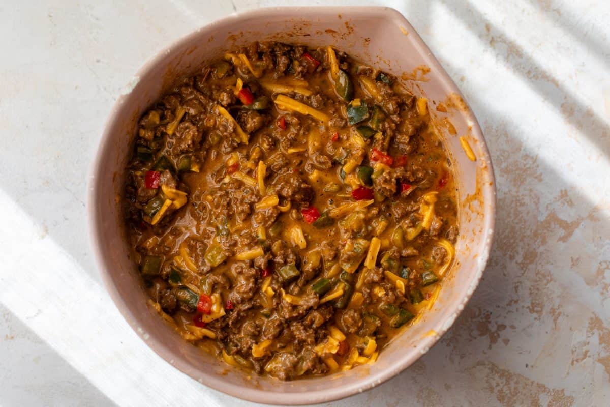 A mixing bowl filled with cheesy ground beef and vegetable mixture, viewed from above.