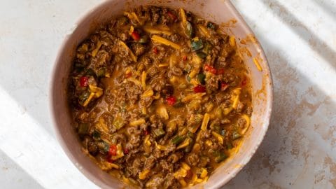 A mixing bowl filled with cheesy ground beef and vegetable mixture, viewed from above.