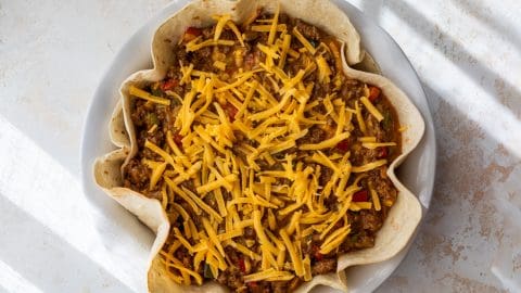 A taco pie filled with seasoned ground beef, vegetables, and topped with shredded cheddar cheese.