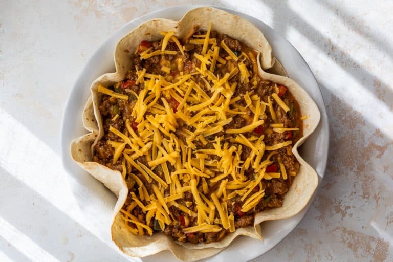 A taco pie filled with seasoned ground beef, vegetables, and topped with shredded cheddar cheese.