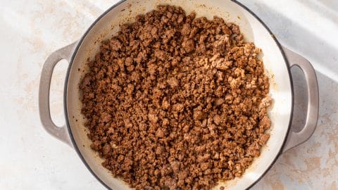 Cooked ground beef with spices in a large white pot, pictured from above on a light-colored surface.