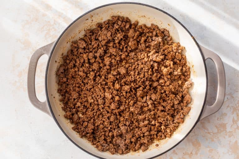 Cooked ground beef with spices in a large white pot, pictured from above on a light-colored surface.