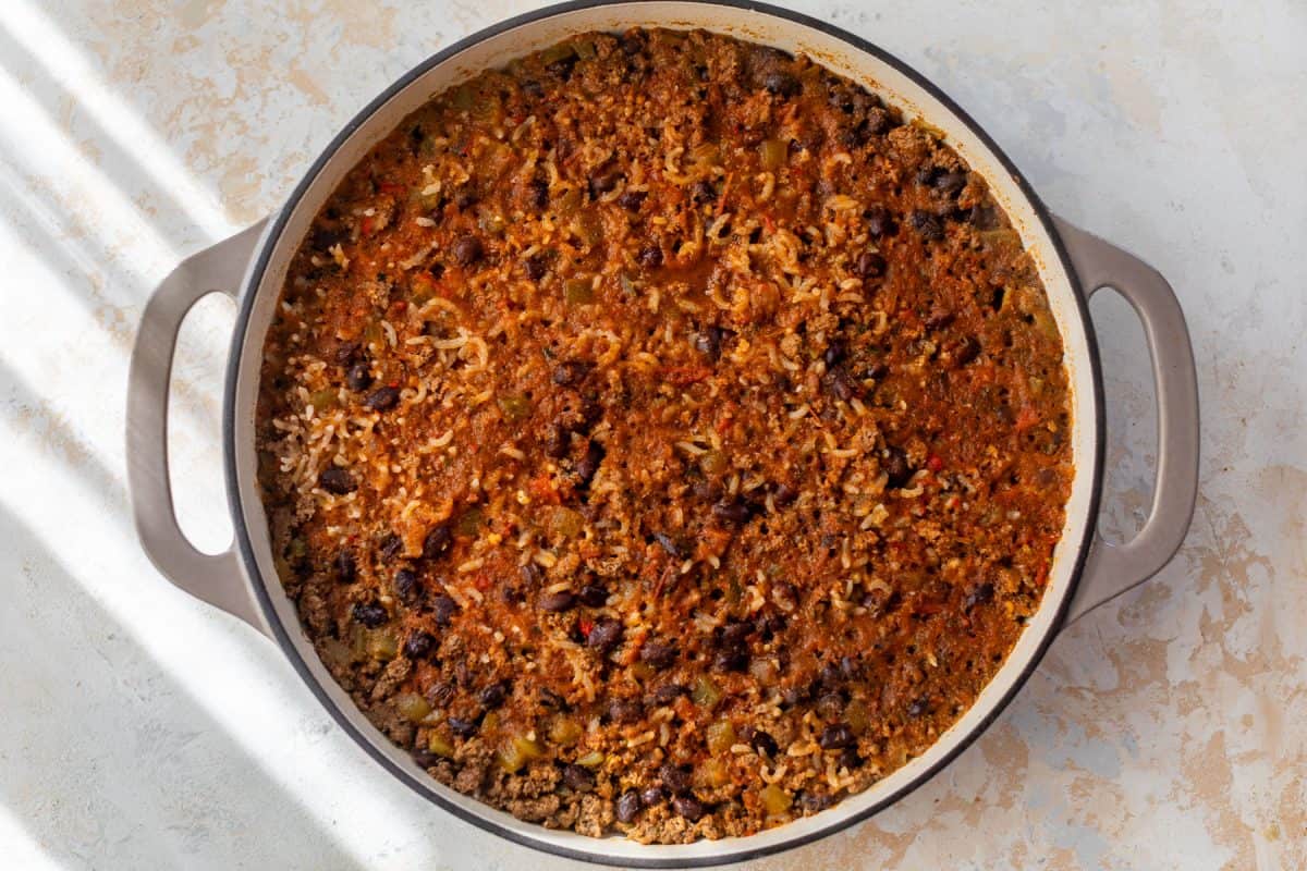 A pot of taco rice with cooked ground beef, black beans, rice, and vegetables in a tomato-based sauce.