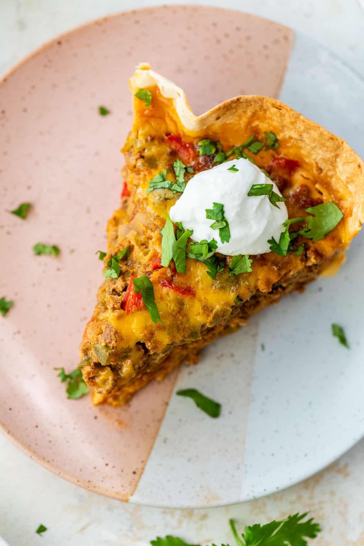 Slice of taco pie topped with sour cream and chopped cilantro on a pink and white plate.