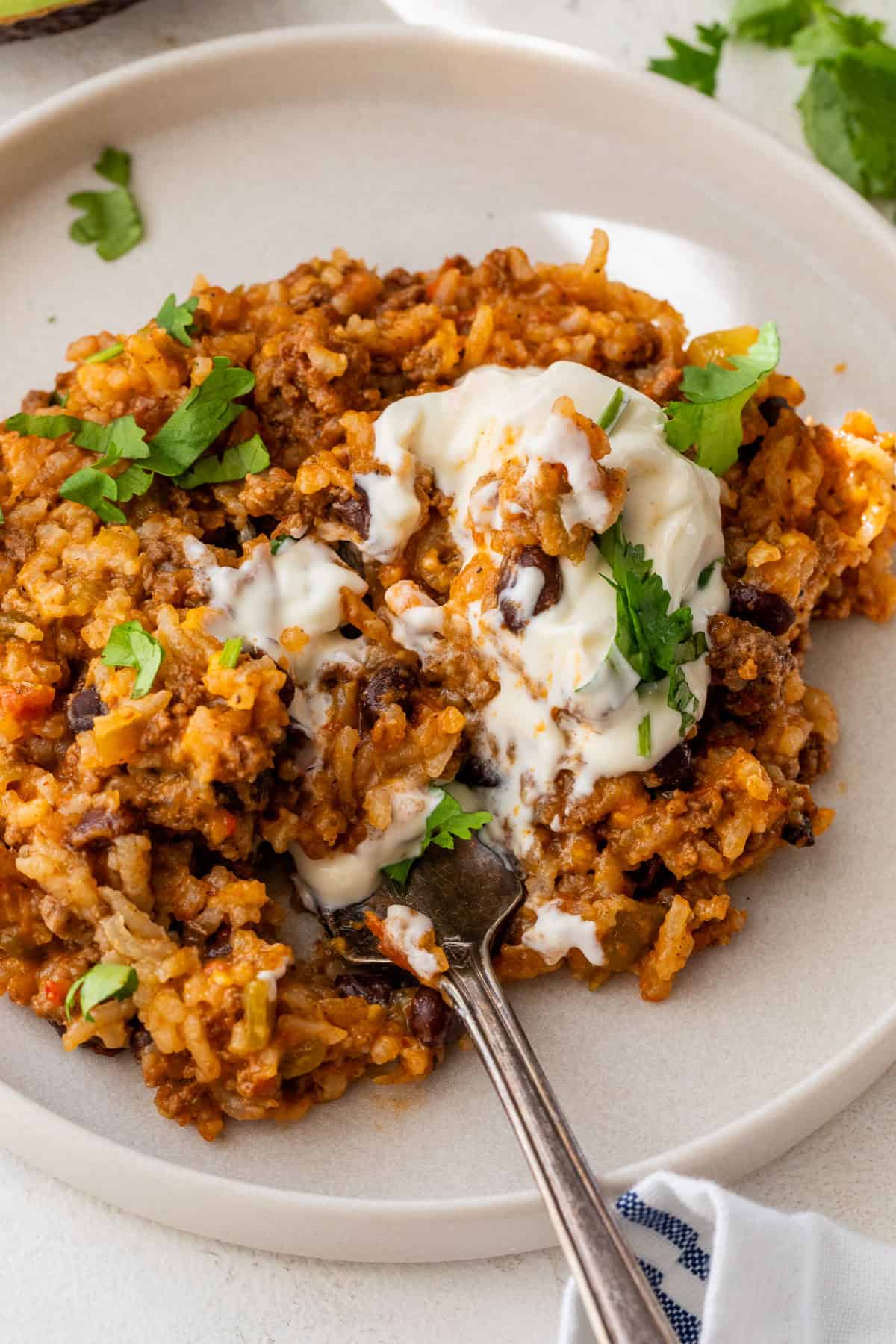 A plate of cheesy taco rice topped with sour cream and fresh cilantro, with a fork resting on the plate.