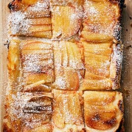 Rectangular upside down apple tart sliced into nine pieces, topped with powdered sugar, on a wooden surface.
