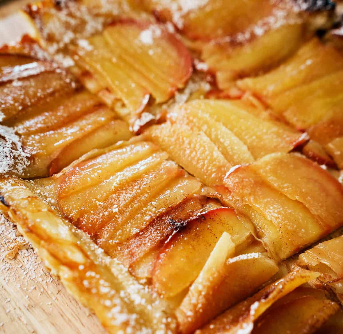 Close-up of a golden brown apple tart with sliced apples and a dusting of powdered sugar on a puff pastry crust