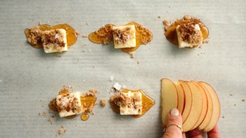 Five butter slices with honey and brown sugar on parchment; hand holding thin apple slices bottom right.