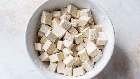 A white bowl filled with cubes of raw tofu dusted with flour.