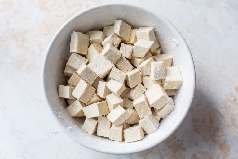 A white bowl filled with cubes of raw tofu dusted with flour.