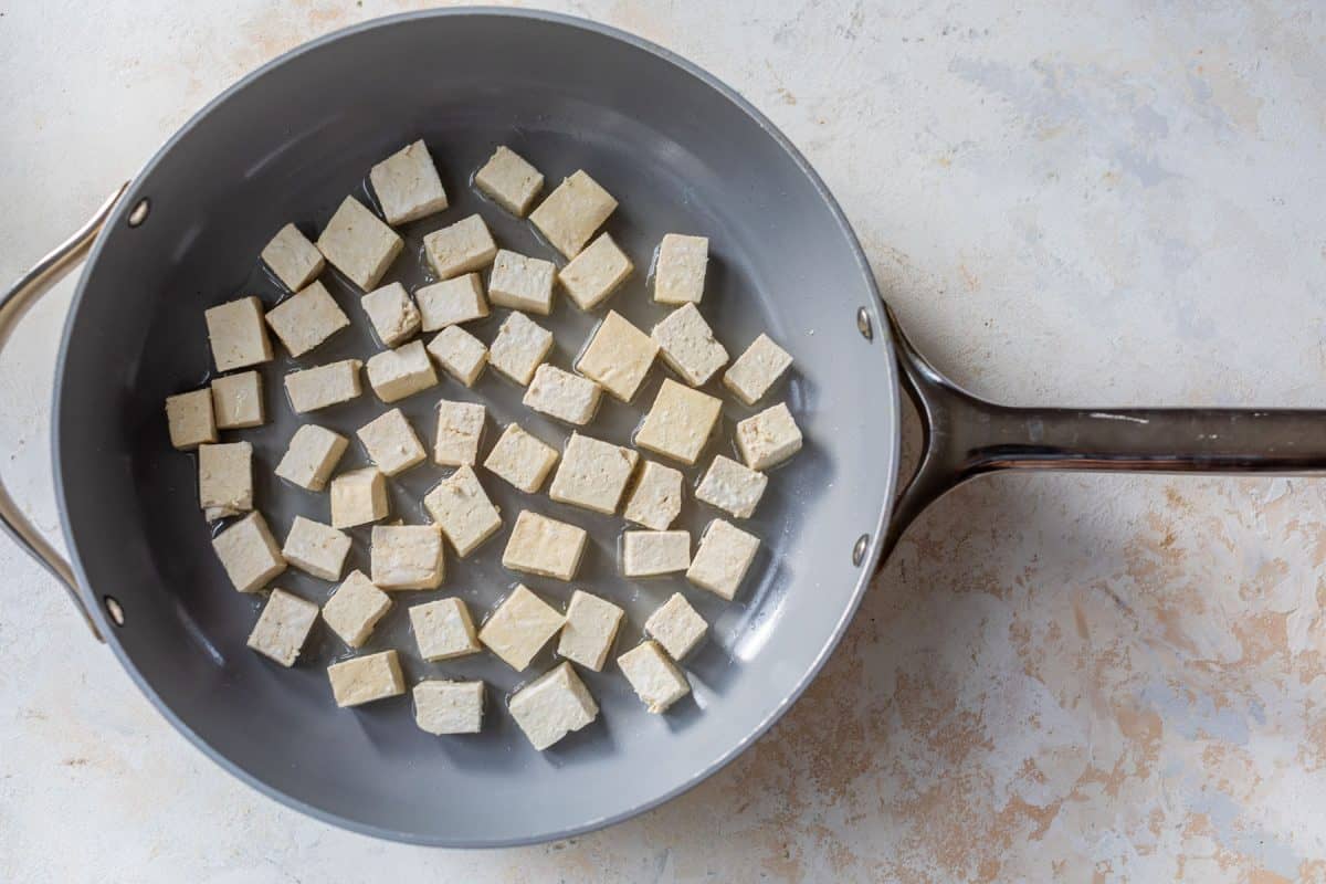 Cubed tofu cooking in a grey skillet.