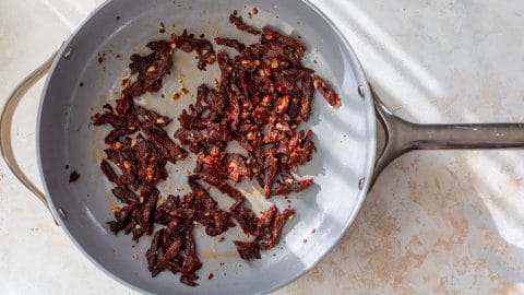 Sun-dried tomatoes and minced garlic cooking in a grey skillet.