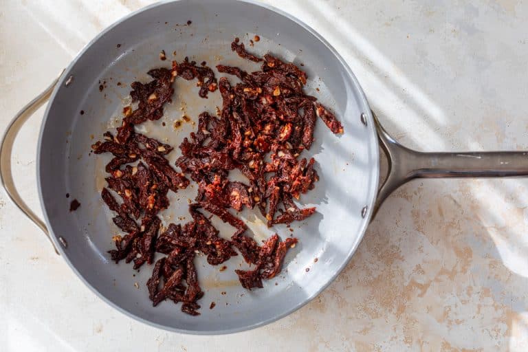 Sun-dried tomatoes and minced garlic cooking in a grey skillet.