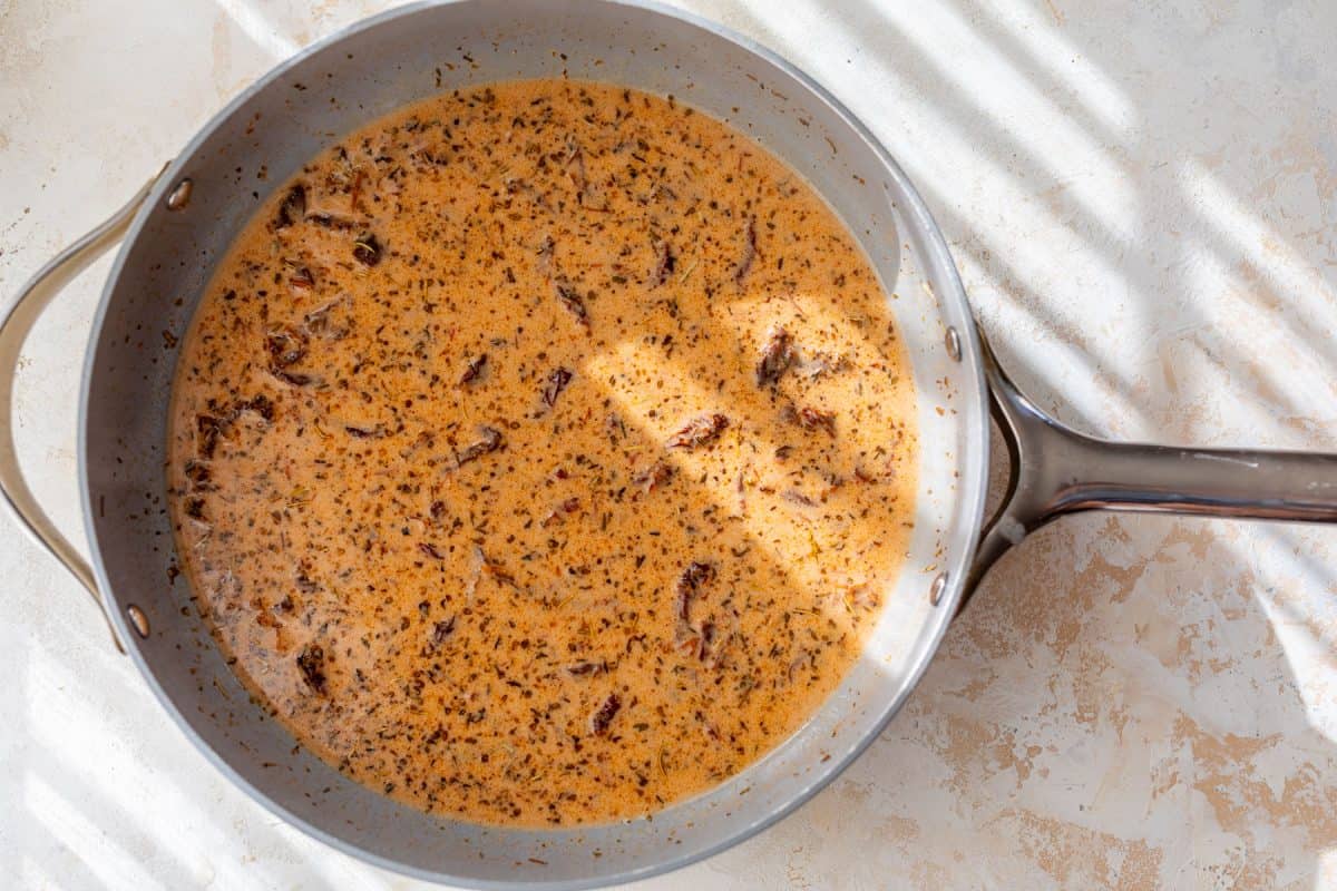 A creamy sun-dried tomato sauce with herbs and sun-dried tomatoes simmering in a skillet.