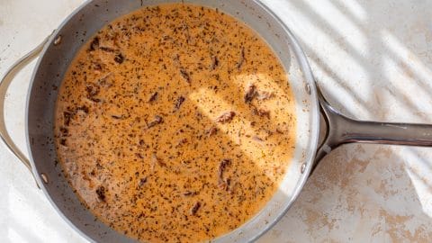 A creamy sun-dried tomato sauce with herbs and sun-dried tomatoes simmering in a skillet.